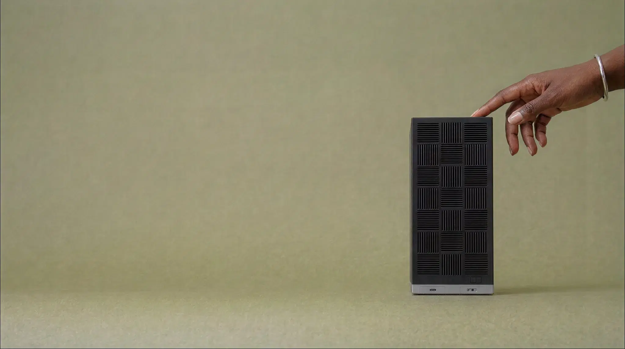 The Box on a sage backdrop, a hand reaching in to touch its top